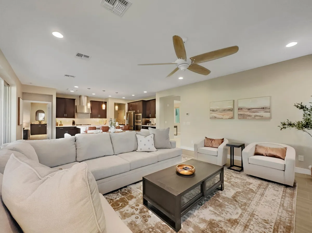 A cozy living room featuring a large sectional sofa, a stylish coffee table, and artwork adorning the walls. The arrangement encourages relaxation, conversation, and entertaining. Sunlight streams in, enhancing the inviting mood and highlighting the chic décor.