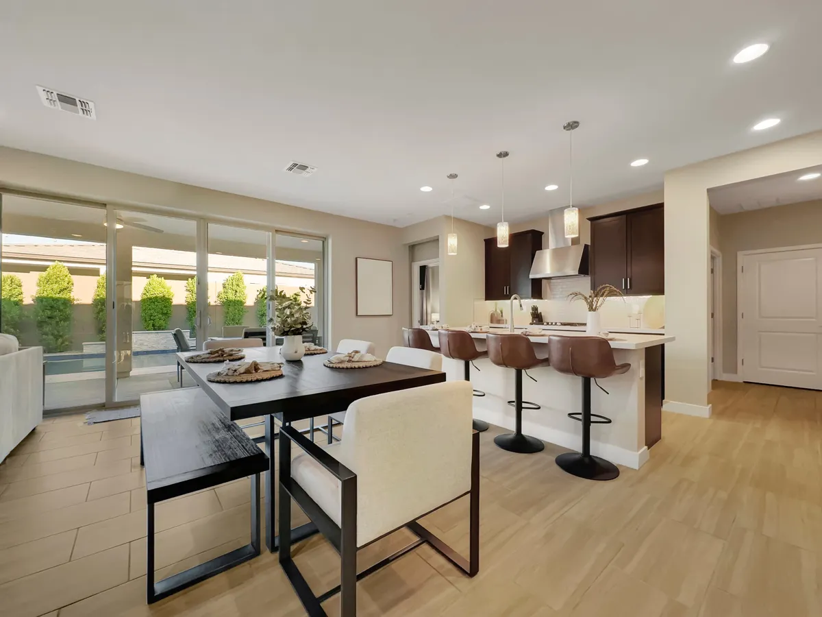 A modern kitchen and dining area with a spacious island, bar stools, and a large dining table. Expansive windows let in abundant sunlight, and the adjoining living space further emphasizes the cohesive, open-concept layout. The combination of sleek finishes and inviting seating areas highlights contemporary comfort.