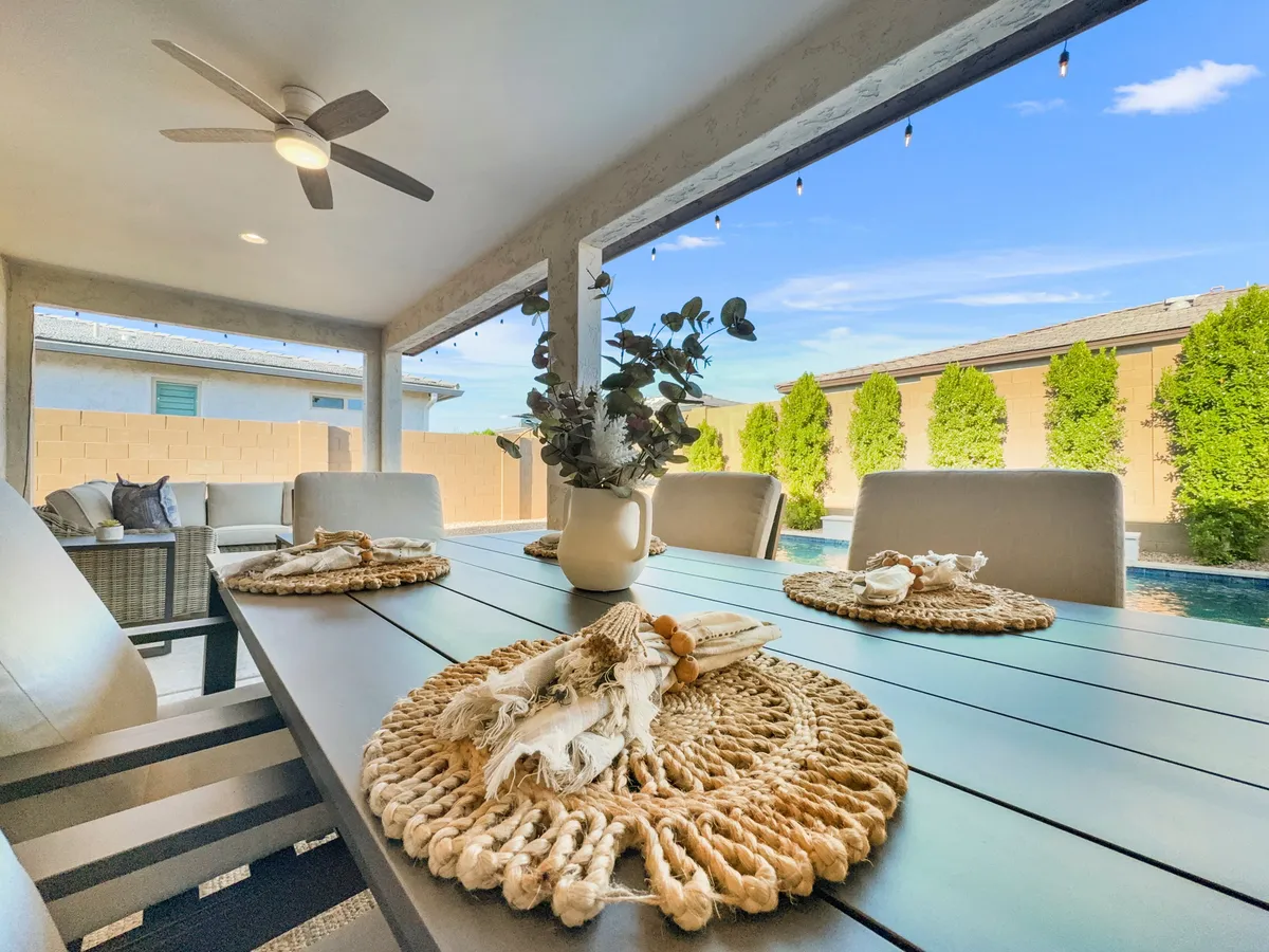 This exterior shot provides a close-up of the outdoor dining table set with decorative placemats and a potted plant, adjacent to a pool and complemented by a stylish outdoor seating area. The scene is bathed in soft light, suggesting casual or sunset dining experiences by the pool.