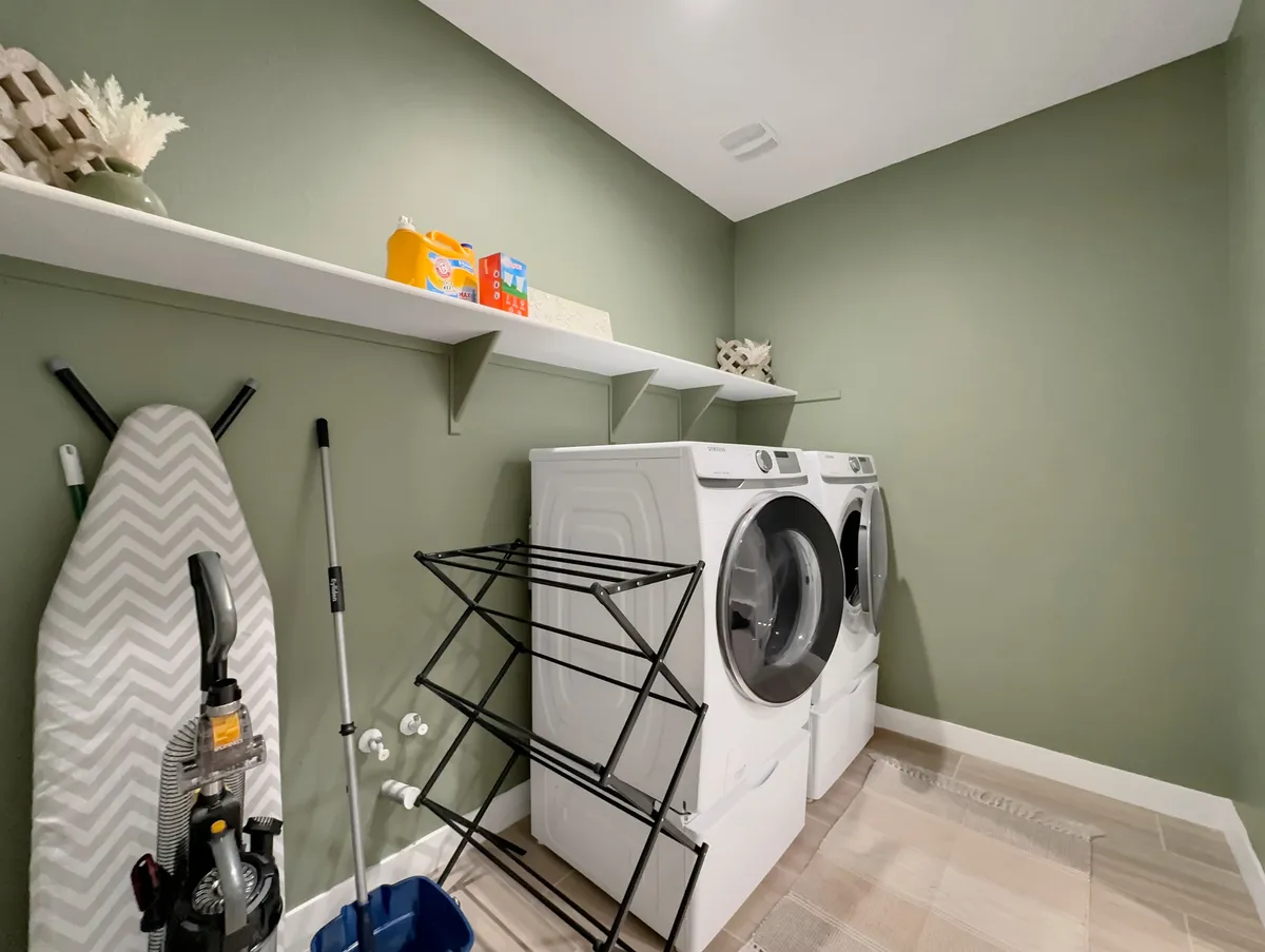 A functional laundry room featuring a washing machine, dryer, ironing board, and clothes drying rack. The space feels clean, organized, and ready for daily use.