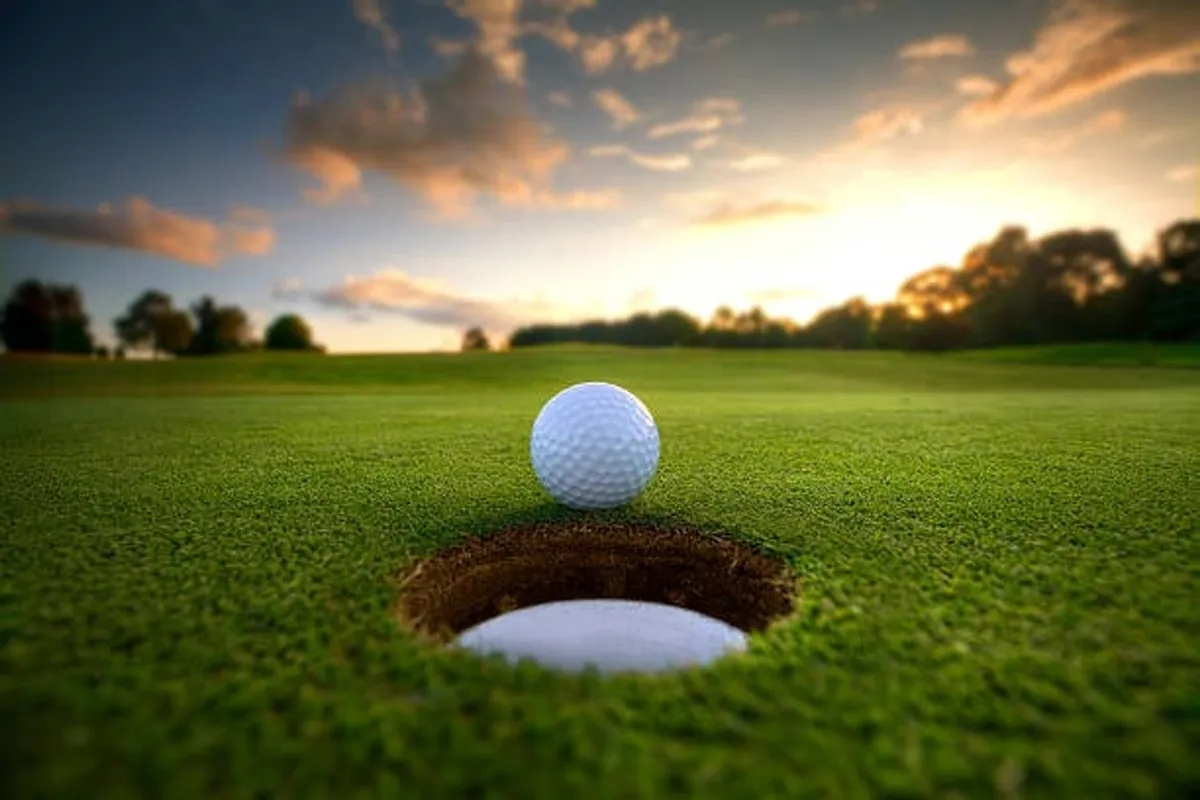 A close-up of a golf ball resting near the hole on a lush green, with vibrant grass and a hint of the course stretching into the distance. The mood is calm and anticipatory, evoking the excitement of a perfect putt.