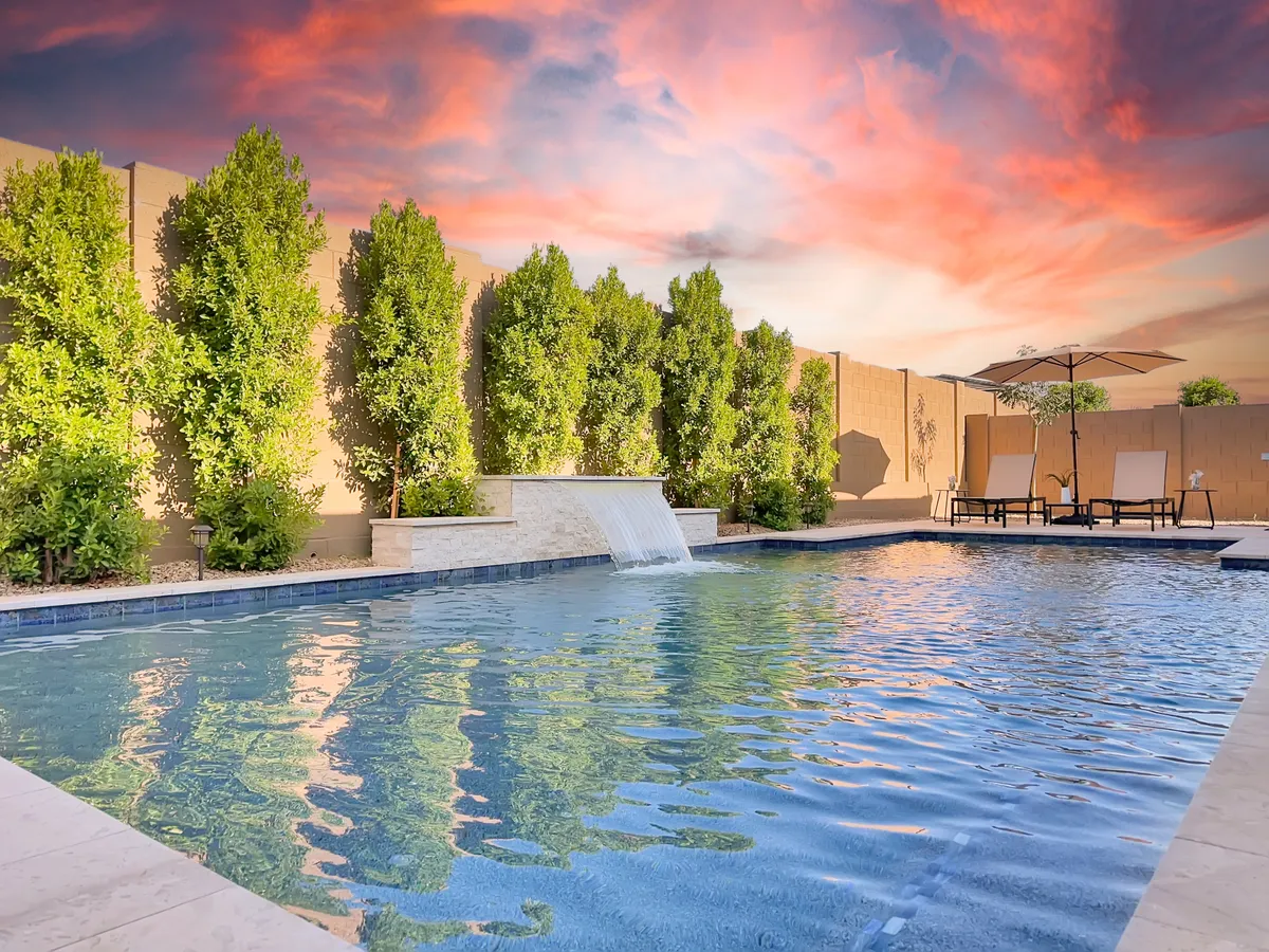 The photo features a tranquil pool area surrounded by lounge chairs and an umbrella, accented by vibrant greenery. The space is perfect for sunbathing, cooling off with a swim, or gathering with friends in a serene setting.