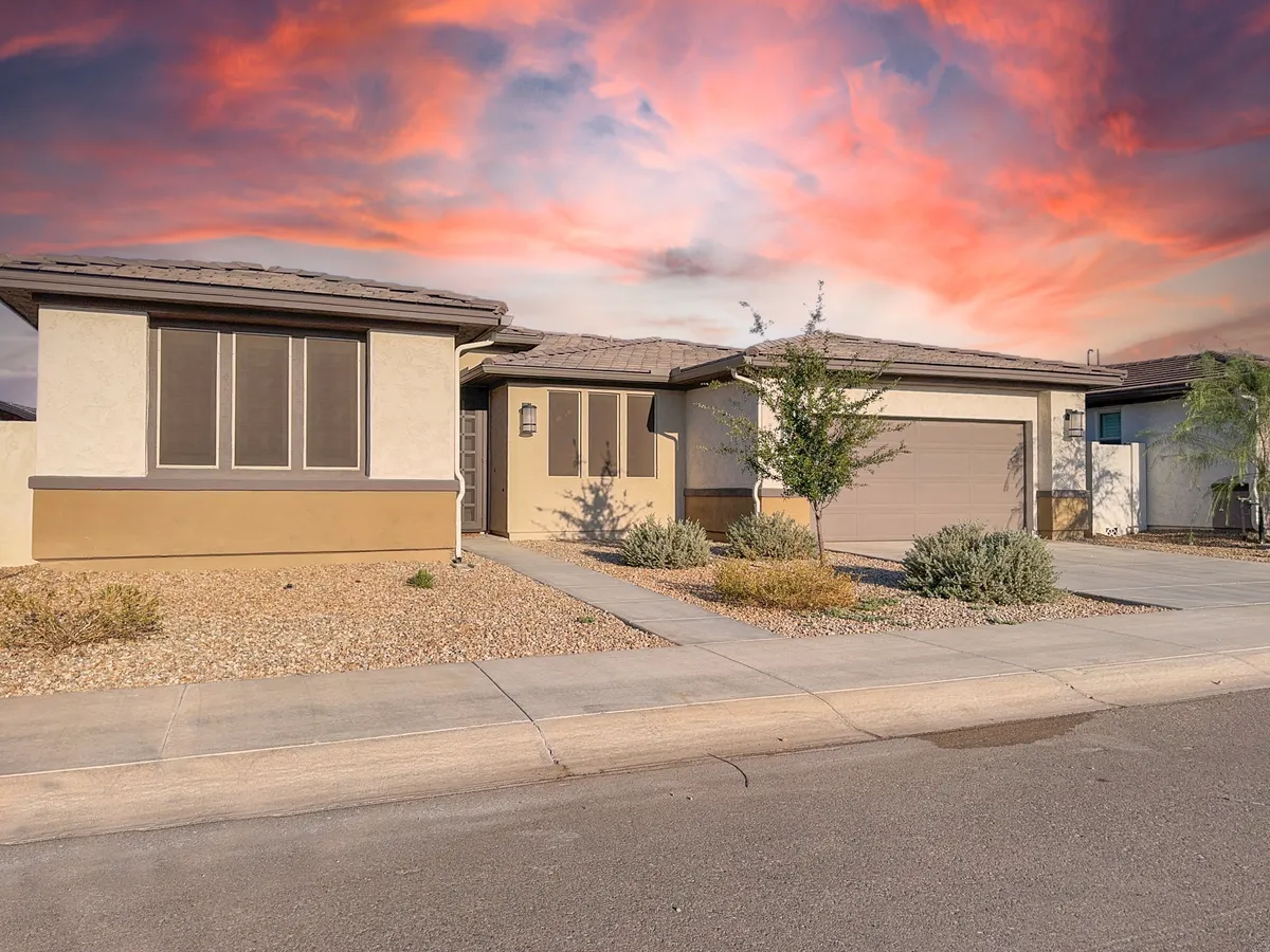 An exterior view showcasing a front entrance with an attached two-car garage, landscaped gravel yard, and a colorful sky in the background. The setting feels welcoming and serene, ideal for both active and retired residents.