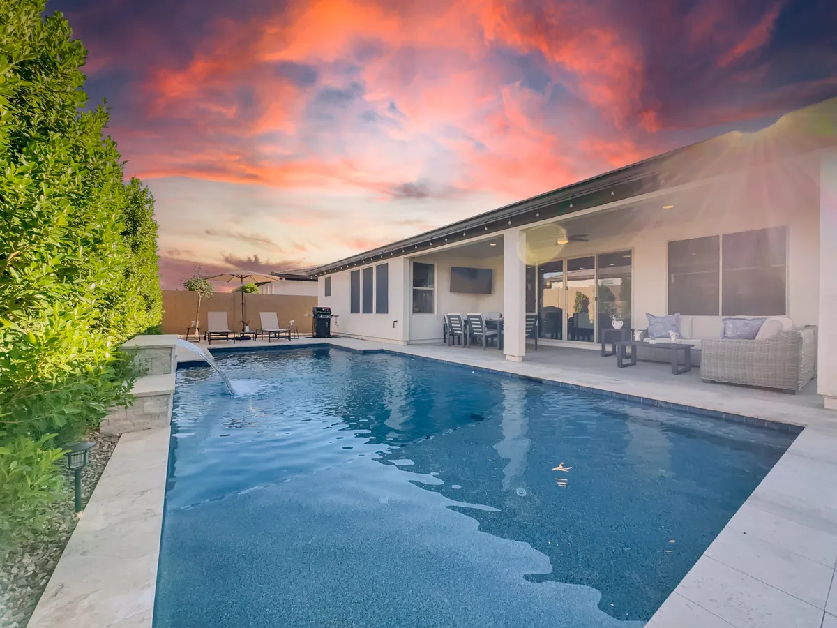 An inviting exterior image featuring a swimming pool, a sunset sky, an outdoor seating area, green hedges, and the house exterior. This scene blends the serenity of evening gatherings with the allure of sunset swims and relaxed lounging.