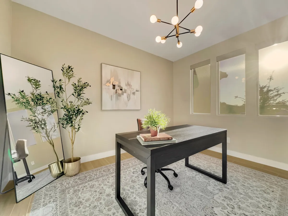 A serene, well-lit home office with a desk arranged with books and a plant, soft lighting from a chandelier, and a mirror reflecting the calm atmosphere. The setting is ideal for focused work, reading, or studying.