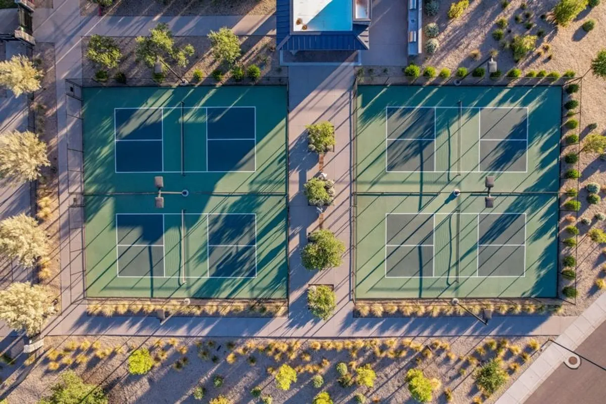 This exterior shot features well-maintained tennis courts framed by landscaped pathways and greenery. The courts are ready for competitive matches or casual play, with open spaces that suggest room for social gatherings and community events.